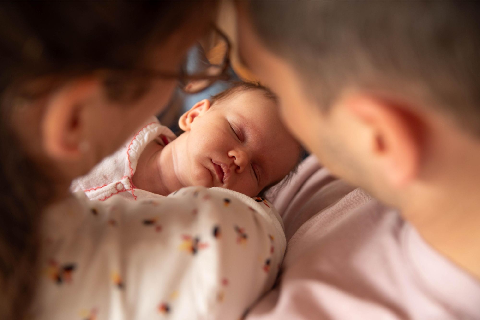 photographie d'un bébé dans les bras de ses parents lors d'une session naissance à domicile