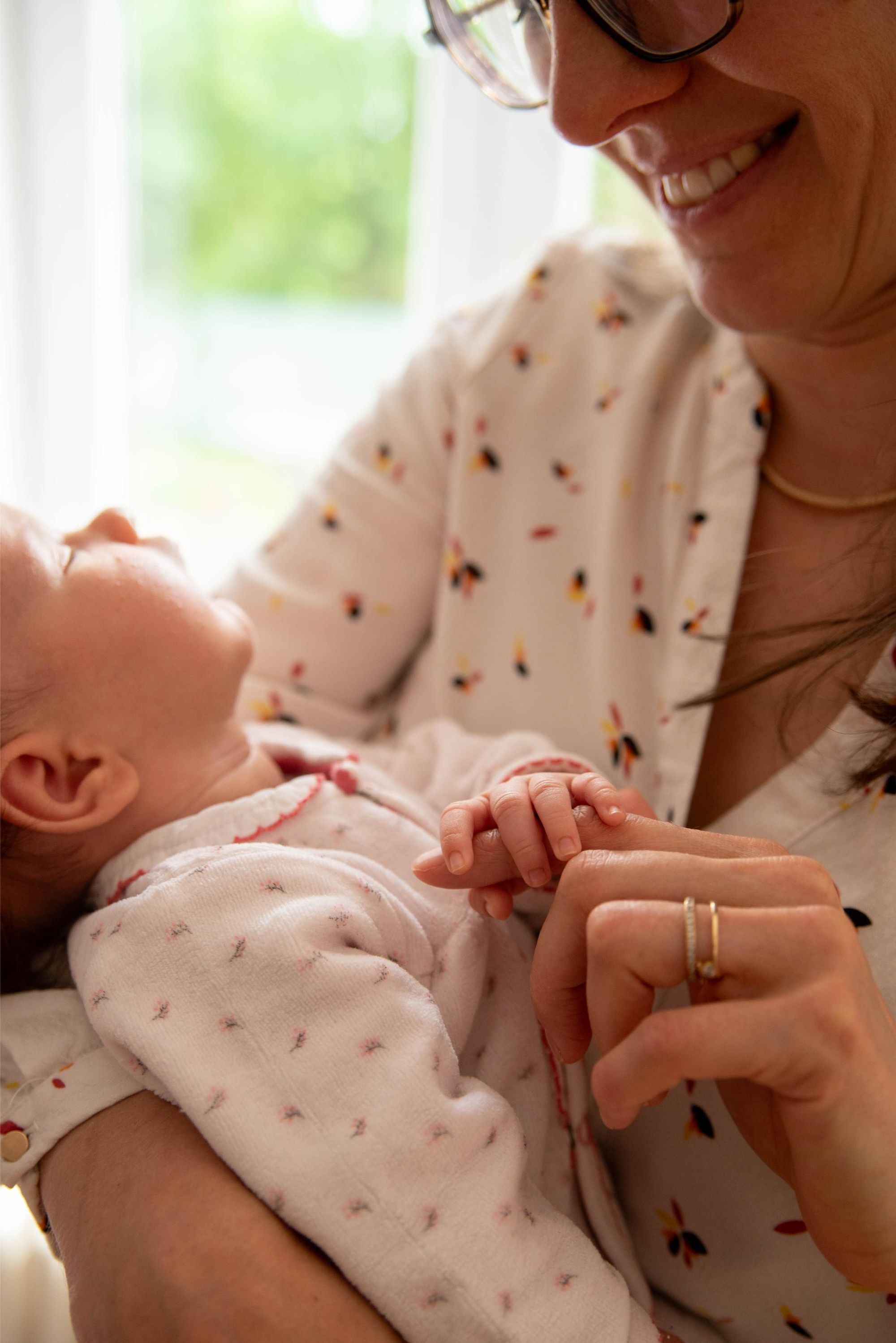 photo d'une petite fille dans les bras de sa maman qui lui tient son doigt lors d'une session naissance à domicile proche de Besançon
