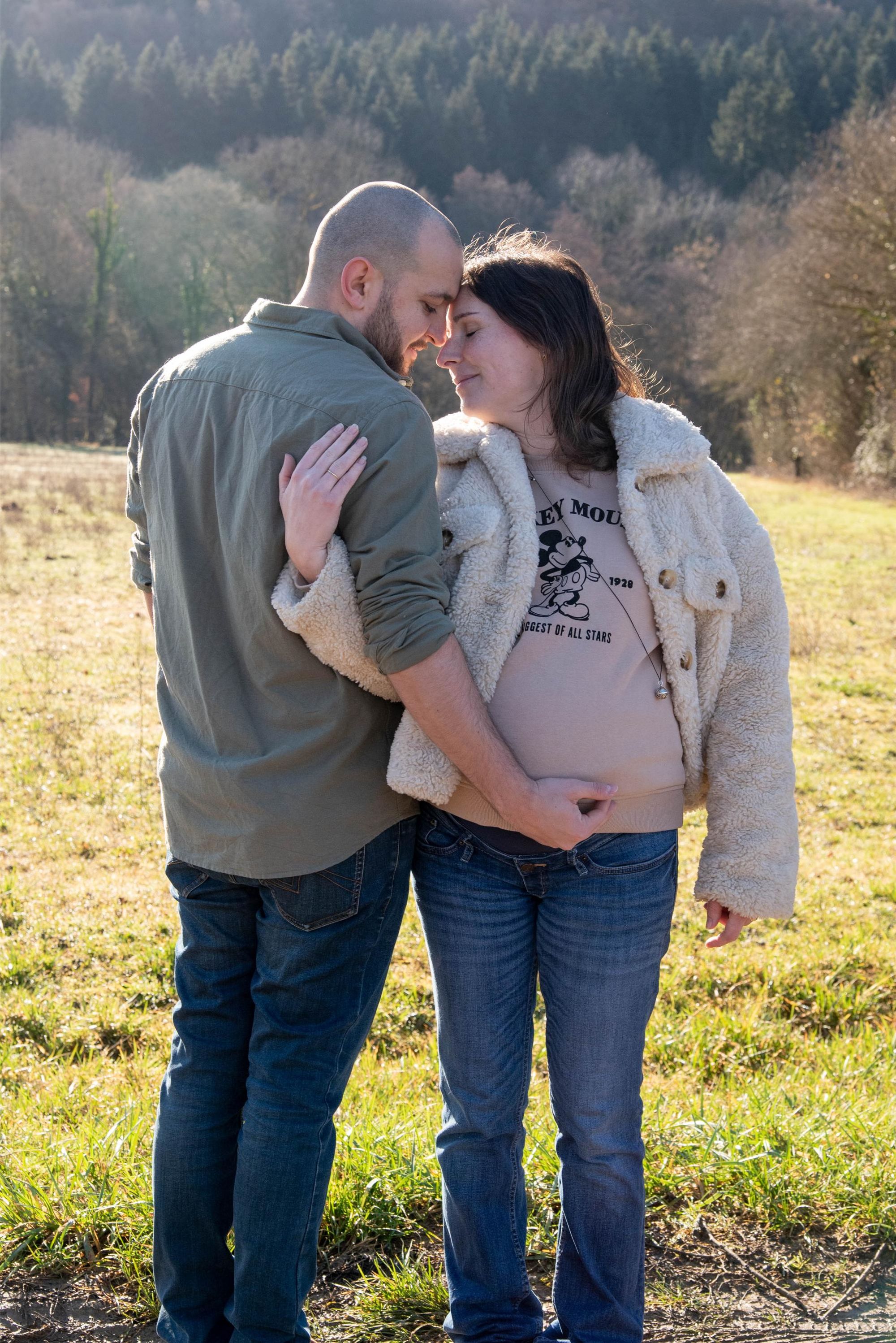 photo d'un couple front contre front lors d'une session couple à Besançon. Le futur papa touche le ventre de sa compagne avec émotion