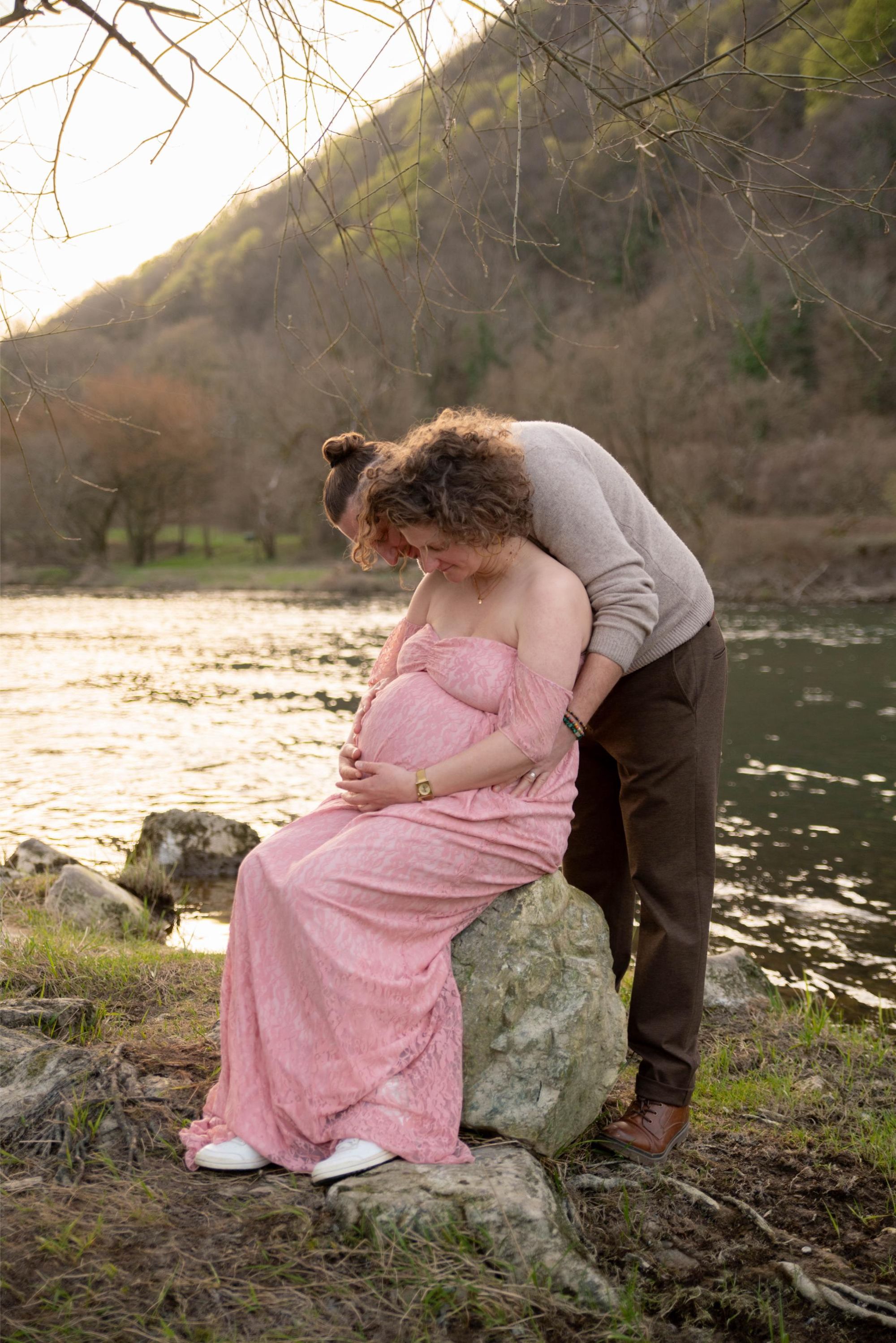 photo d'une future maman et son conjoint lors d'une session photo grossesse. la future maman est assise au bord de l'eau en extérieur proche de Besançon