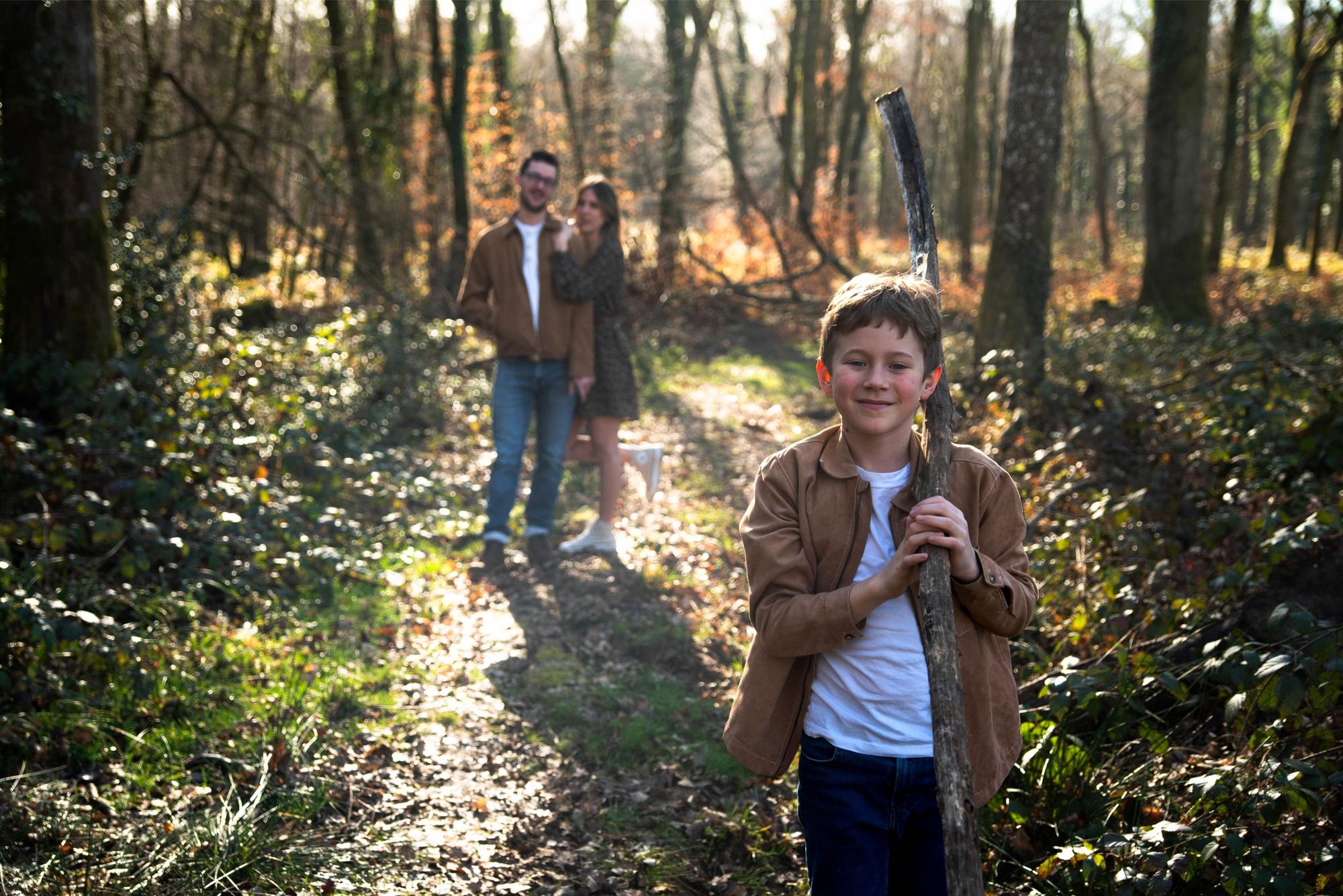 photo d'un petit garçon qui pose, ses parents sont en arrière plan, lors d'une session famille en foret à Besançon