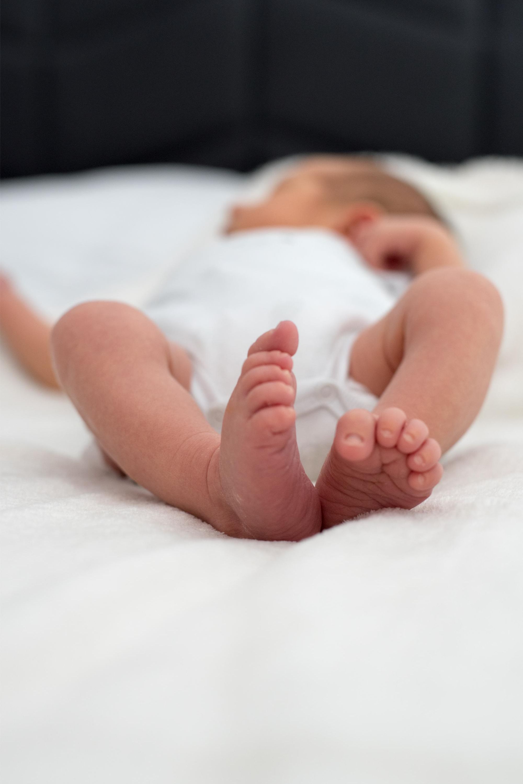 bébé allongé sur le lit tout en blanc lors d'une session photo naissance, détail sur les pieds, à Besançon