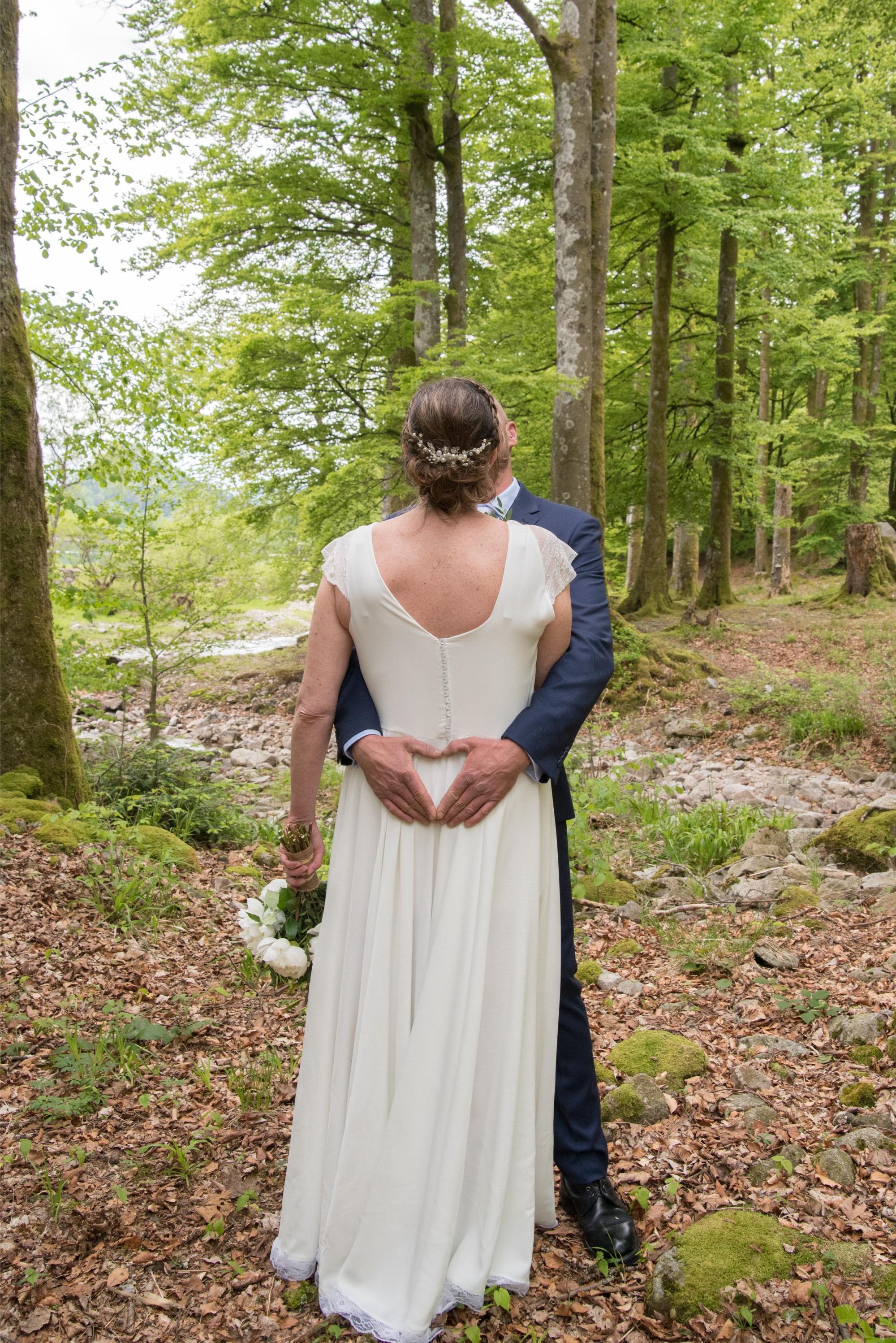 photo de mariage bohème chic, session couple dans la foret. mariée de dos, main du marié forme un coeur, dans le grand est