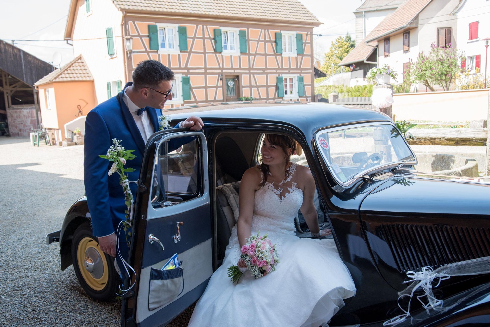 mariés lors de la séance couple. la mariée est assise dans une voiture ancienne, son mari la regarde amoureusement, dans le grand est