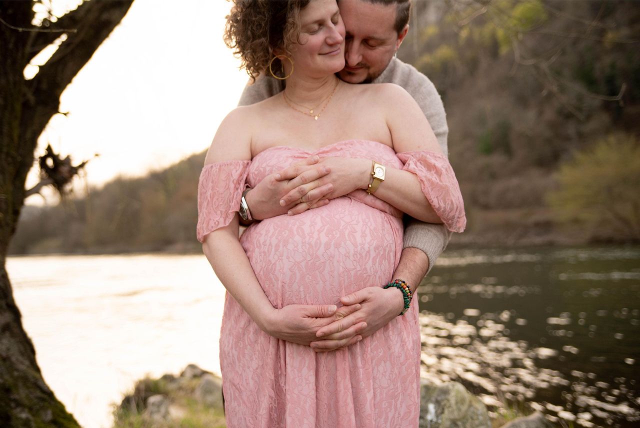 photo d'un ventre de femme enceinte lors d'une séance grossesse au bord de l'eau avec son conjoint