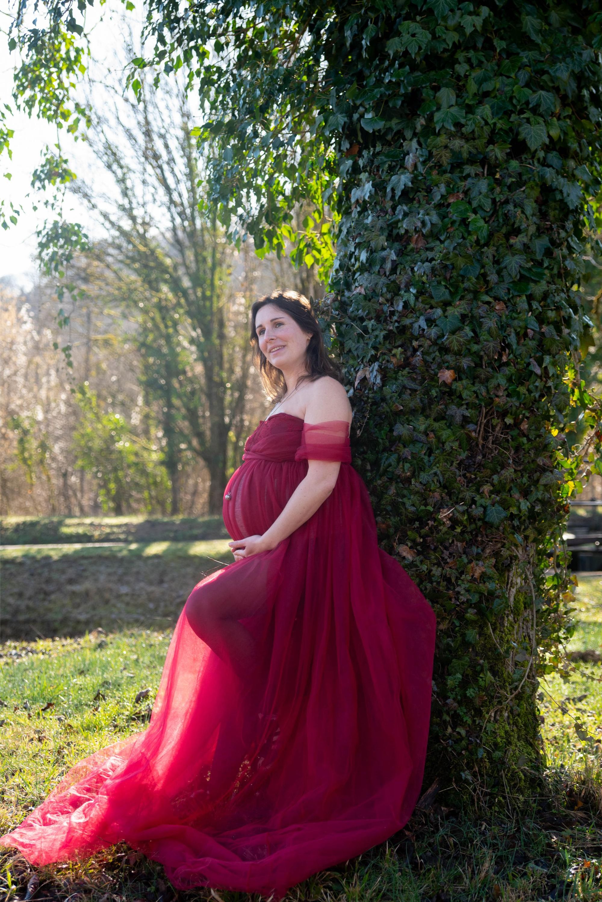 future maman lors d'une session photo de grossesse qui sourit, habillé avec une robe de grossesse rouge, la session a lieu à Besançon